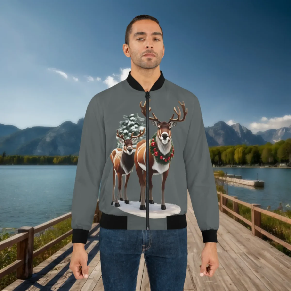 Man wearing a grey bomber jacket with a festive design of two reindeer standing in snow, one decorated with a Christmas wreath, set against a scenic lake and mountain background.