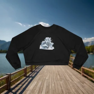 Black cropped sweatshirt with a frosted snowy tree design laid flat on a wooden dock by a mountain lake.