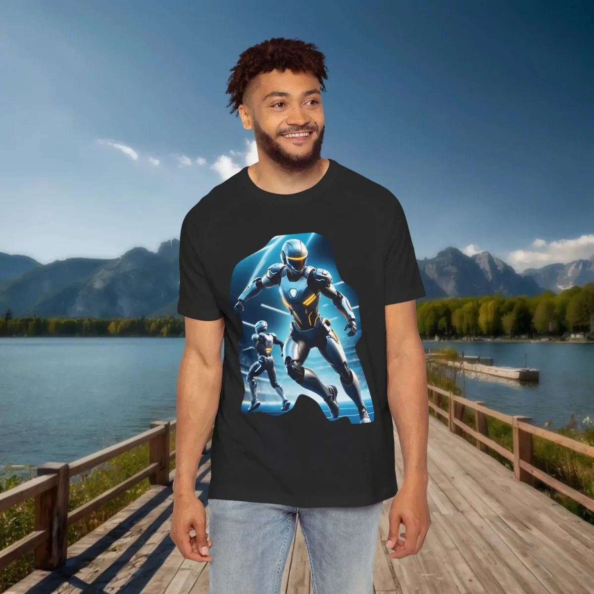 Man wearing a black raglan t-shirt featuring a dynamic illustration of futuristic armored figures, standing on a boardwalk with a lake and mountain landscape in the background.