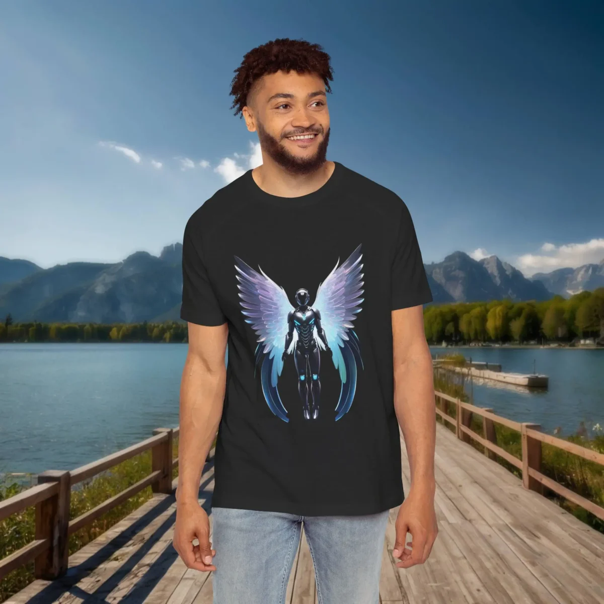 Man wearing a black raglan t-shirt with a glowing winged humanoid illustration, standing outdoors on a wooden dock with water and mountains behind.
