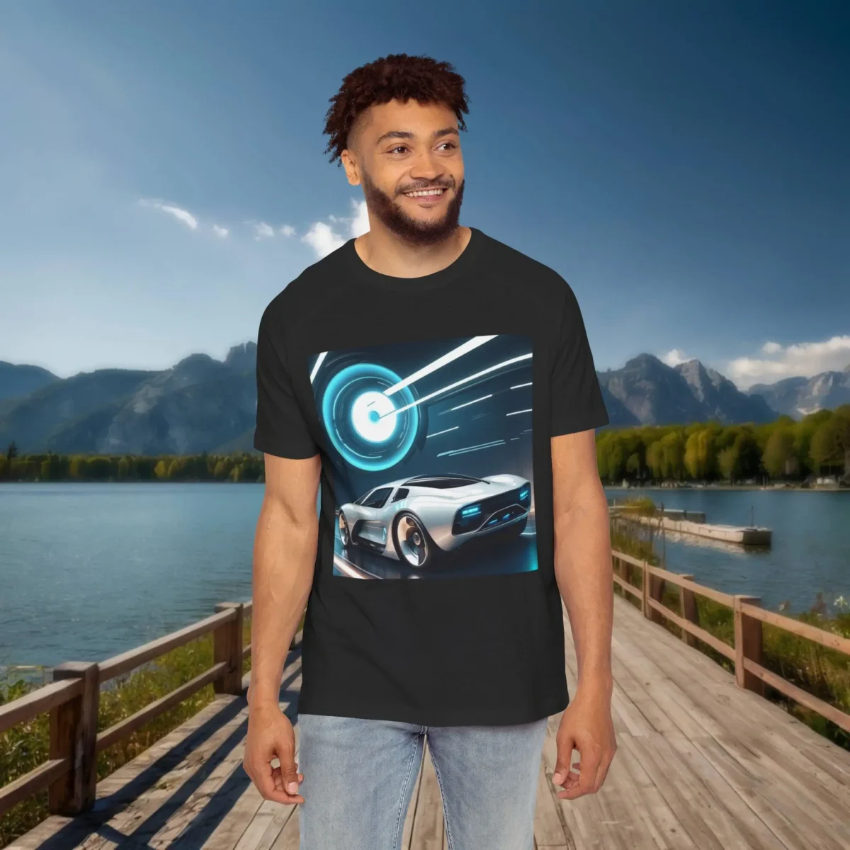 Man wearing a black raglan t-shirt with a retro-futuristic sports car design and glowing digital background, standing on a dock with lake and mountain scenery behind.