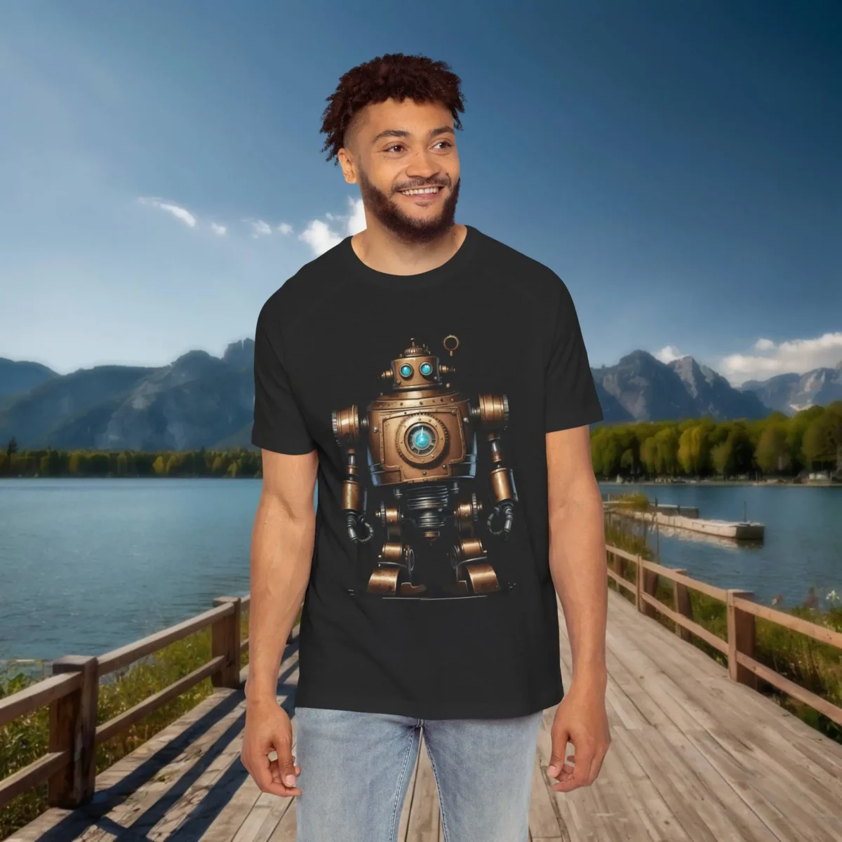 Man wearing a black raglan t-shirt featuring a vintage-style bronze robot with blue eyes and mechanical details, standing on a dock with a lake and mountain view.