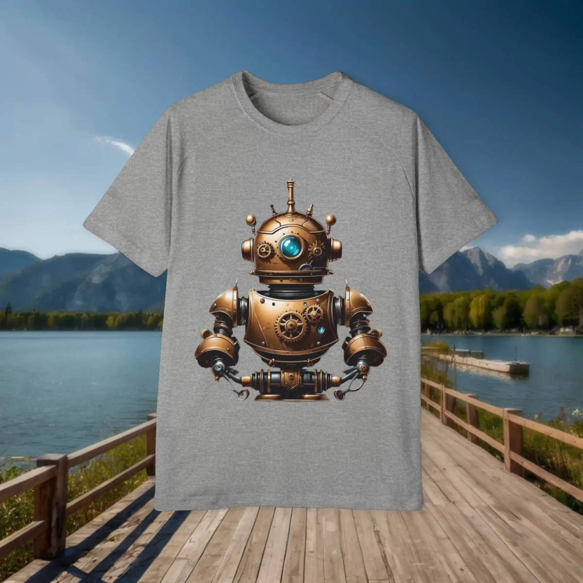 Flat lay of a grey t-shirt displaying a central bronze retro robot design with blue highlights, placed on a wooden dock with lake and mountain view.
