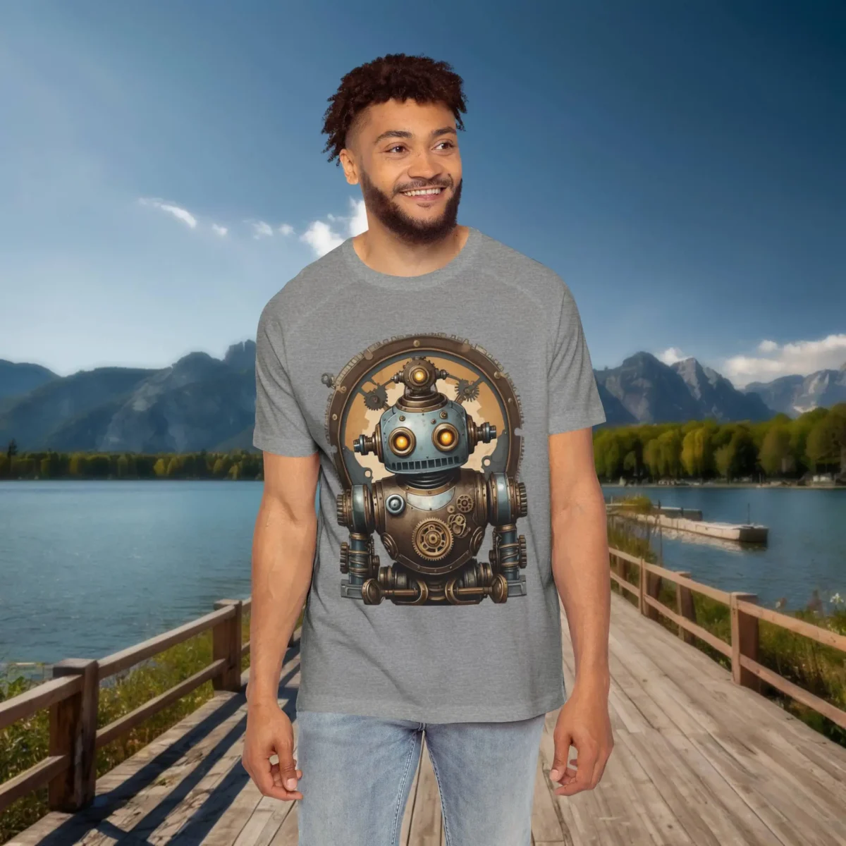 Man wearing a grey raglan t-shirt with a steampunk robot illustration featuring gears, bolts, and glowing eyes, set against a mountain lake backdrop.