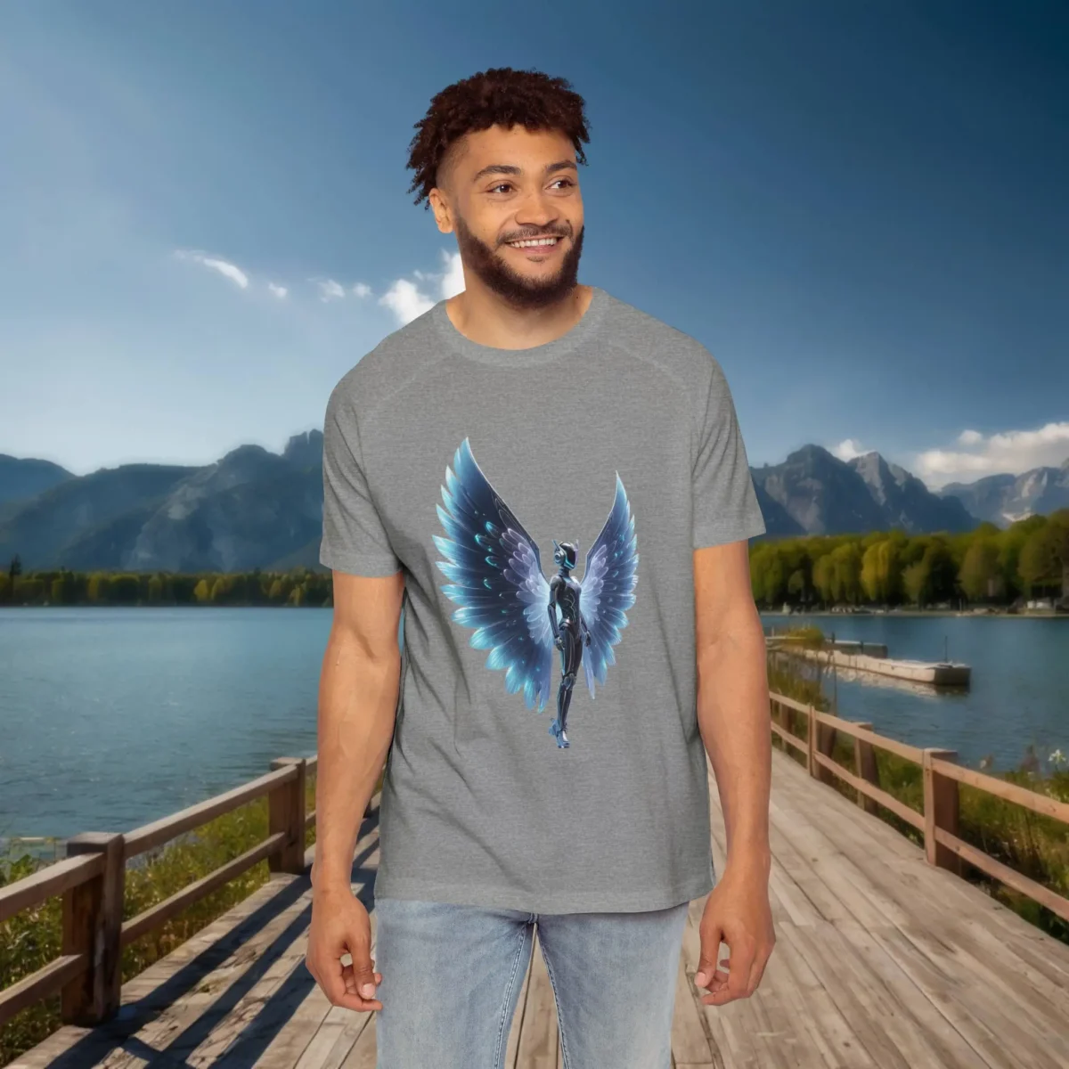 Man wearing a grey raglan t-shirt with a futuristic female figure featuring glowing blue and purple wings, standing on a wooden dock with lake and mountain backdrop.