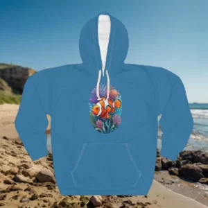 A hoodie featuring a colorful clownfish surrounded by coral reef elements, displayed against a beach background.