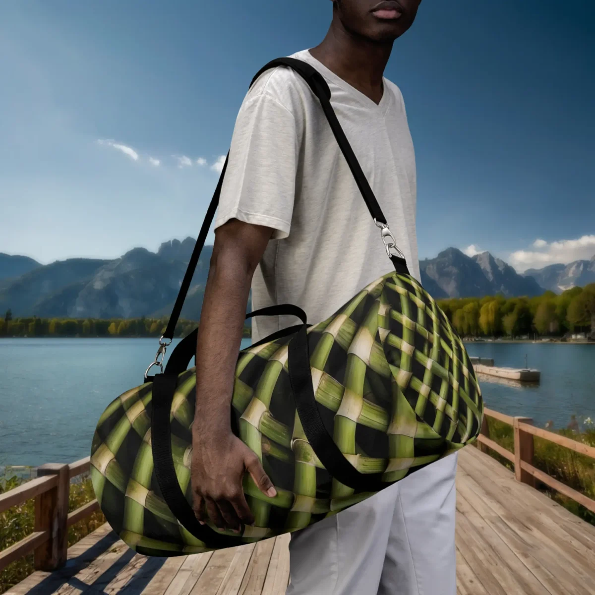 Man holding a large duffel bag with green bamboo weave print on a lakeside boardwalk.