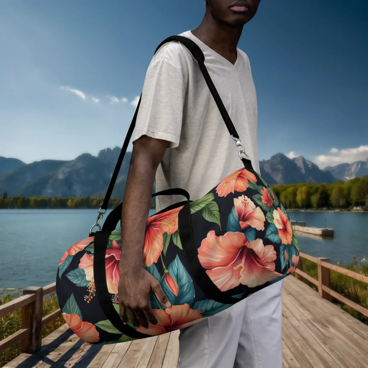Man carrying a large tropical duffel bag with orange hibiscus print on black background near a lake.