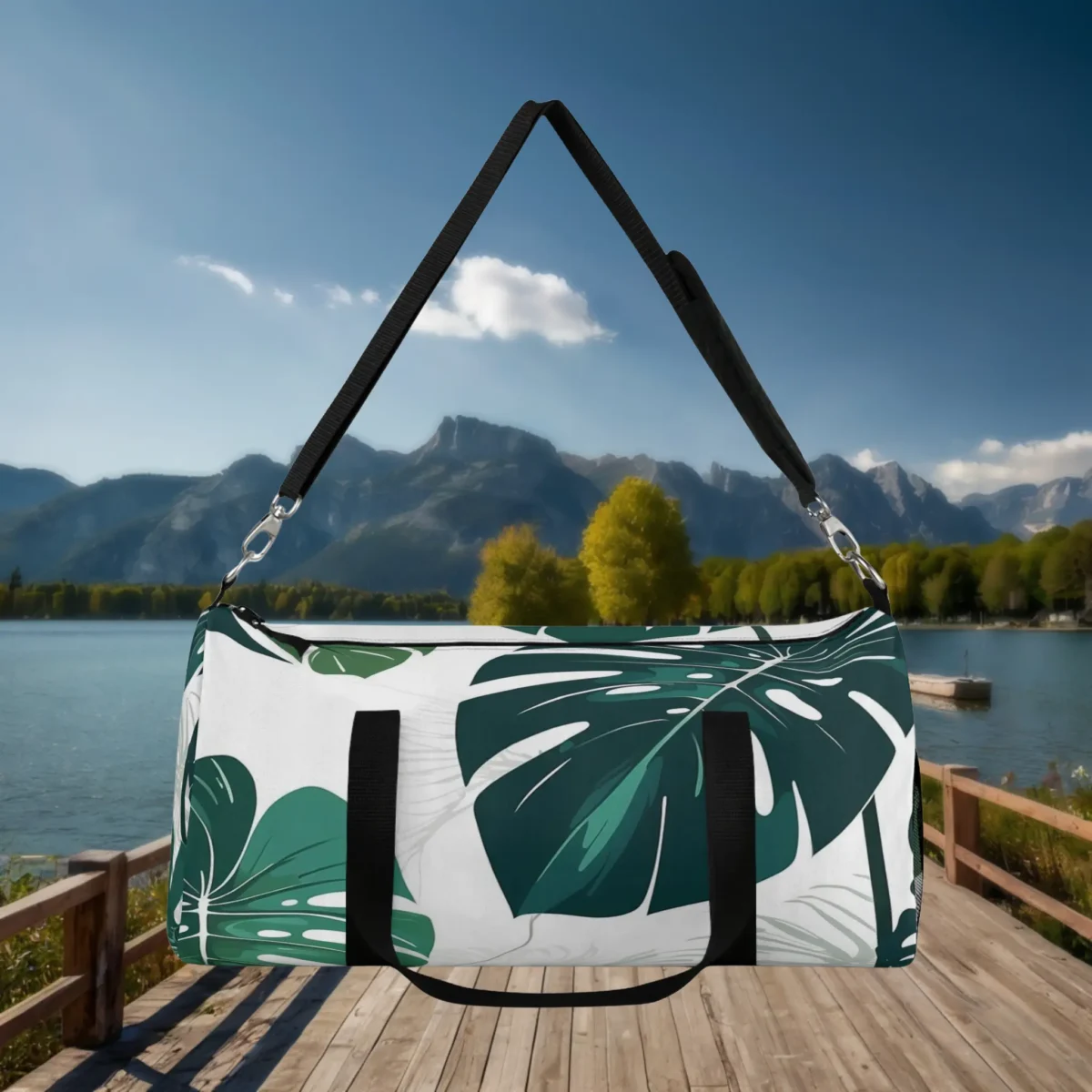 Front view of a large white duffel bag with green monstera leaf print, hanging by its black strap.