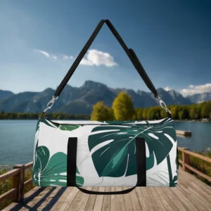 Front view of a large white duffel bag with green monstera leaf print, hanging by its black strap.