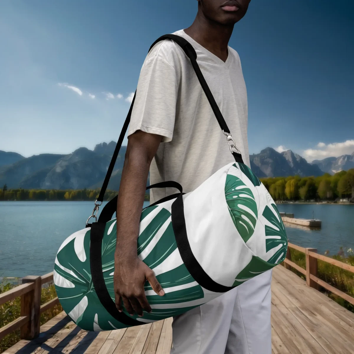 Man holding a large white duffel bag with green monstera print, worn crossbody on a dock.