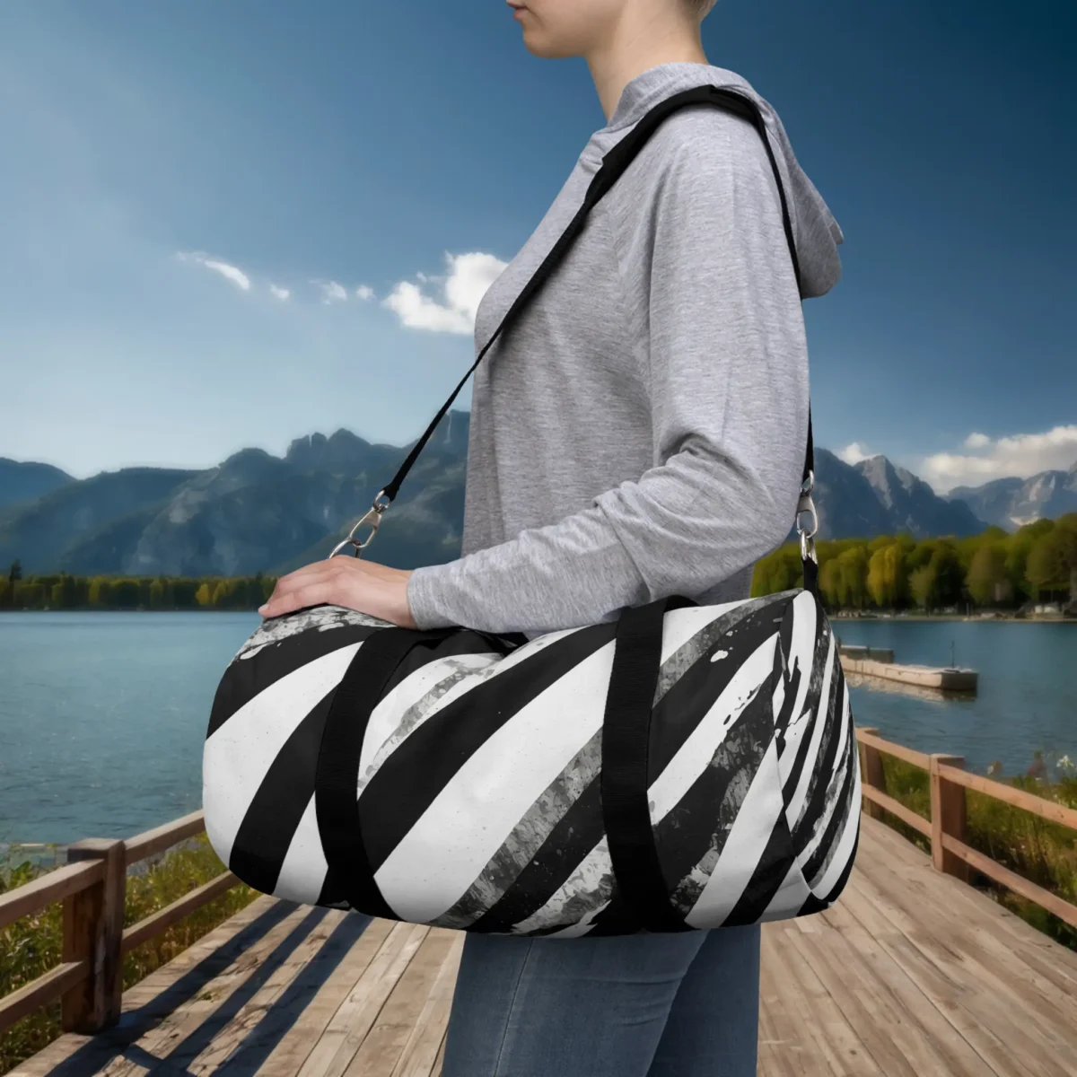 Person carrying a small black and white striped abstract duffel bag with shoulder strap, standing on a lakeside dock.