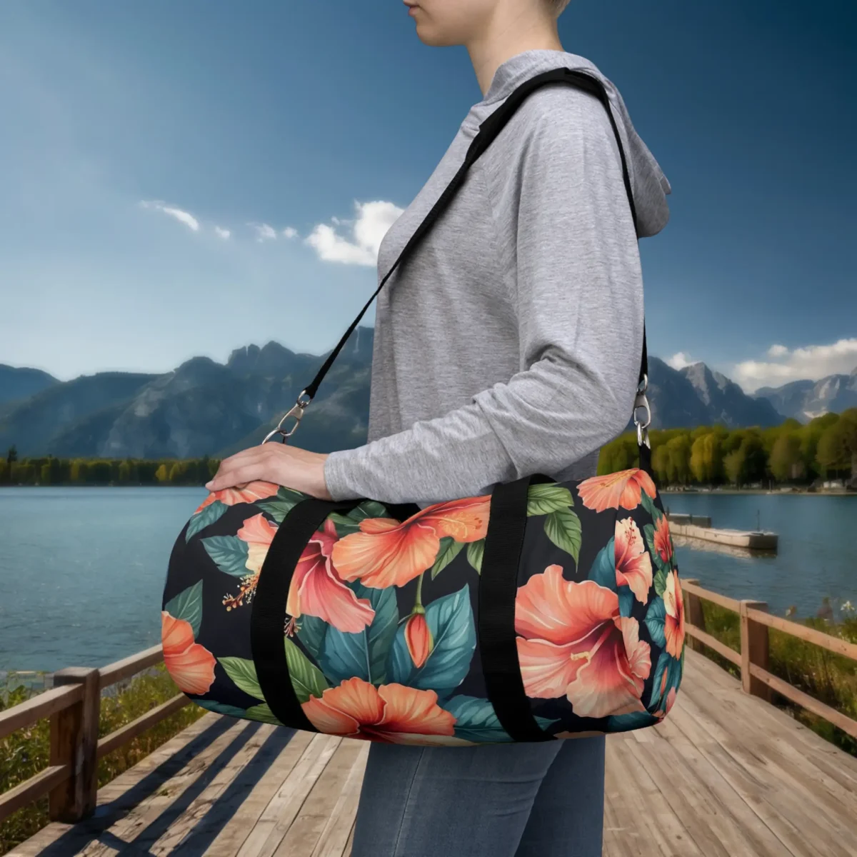 Person wearing a small duffel bag with orange hibiscus flower print on black background, outdoors by a lake.