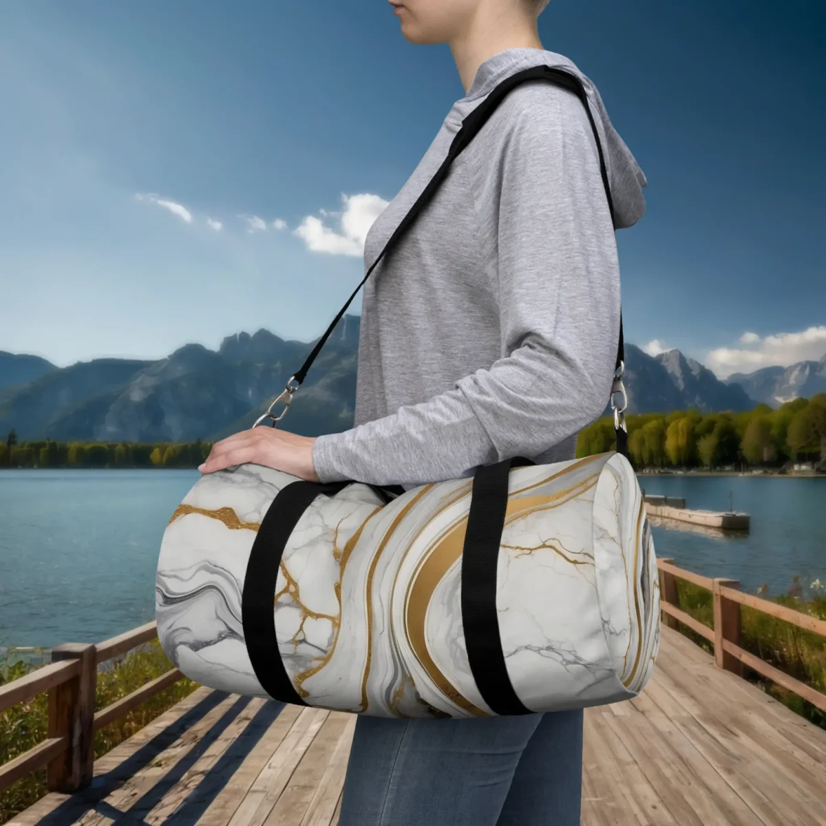 Person carrying a small white marble-pattern duffel bag with gold and grey veins on a dock by the lake.