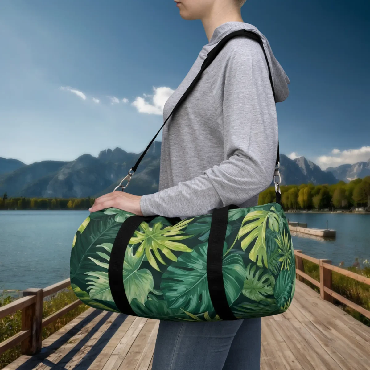 Woman carrying a small duffel bag with green tropical leaf pattern and black straps.