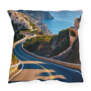 outdoor pillow featuring a winding coastal road with a cliffside village and blue sea