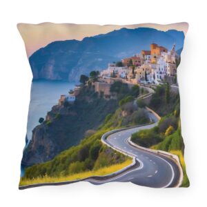 outdoor pillow featuring a winding coastal road leading to a hilltop village with mountains and sea in the background