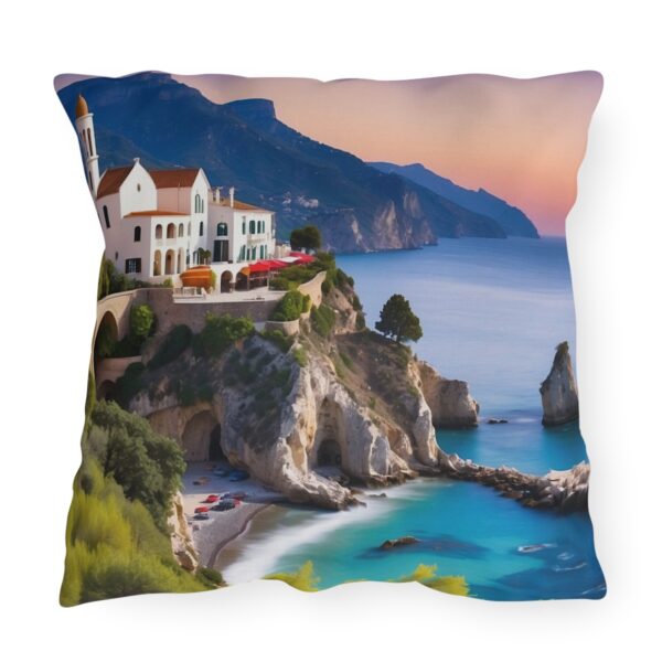 outdoor pillow with a coastal village scene with a cliffside villa, turquoise waters, and a mountainous backdrop