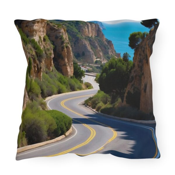 Outdoor pillow featuring a scenic route with winding road through rocky cliffs and greenery by the sea.