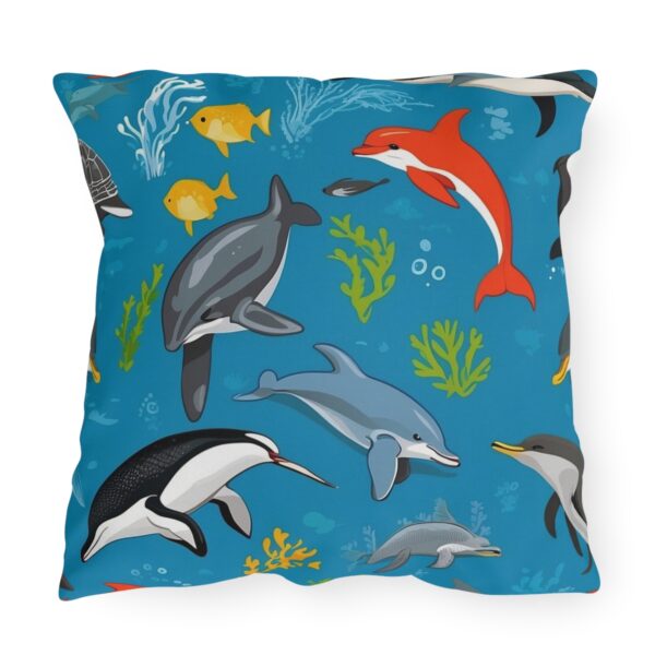 outdoor pillow featuring dolphins, penguins, tropical fish, and sea plants on a bright blue ocean background