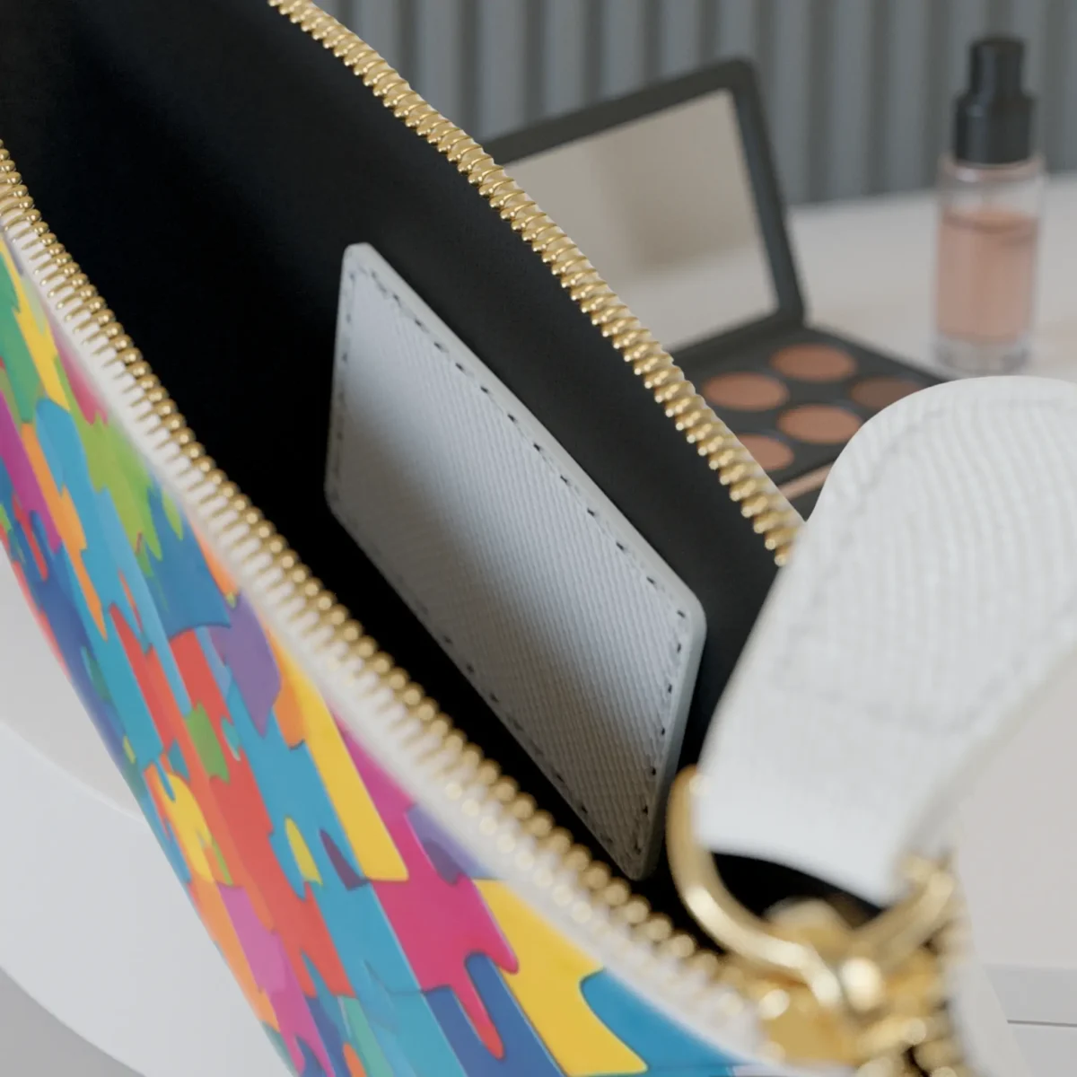 Close-up of colorful puzzle pattern mini clutch bag with zip open to show interior pocket