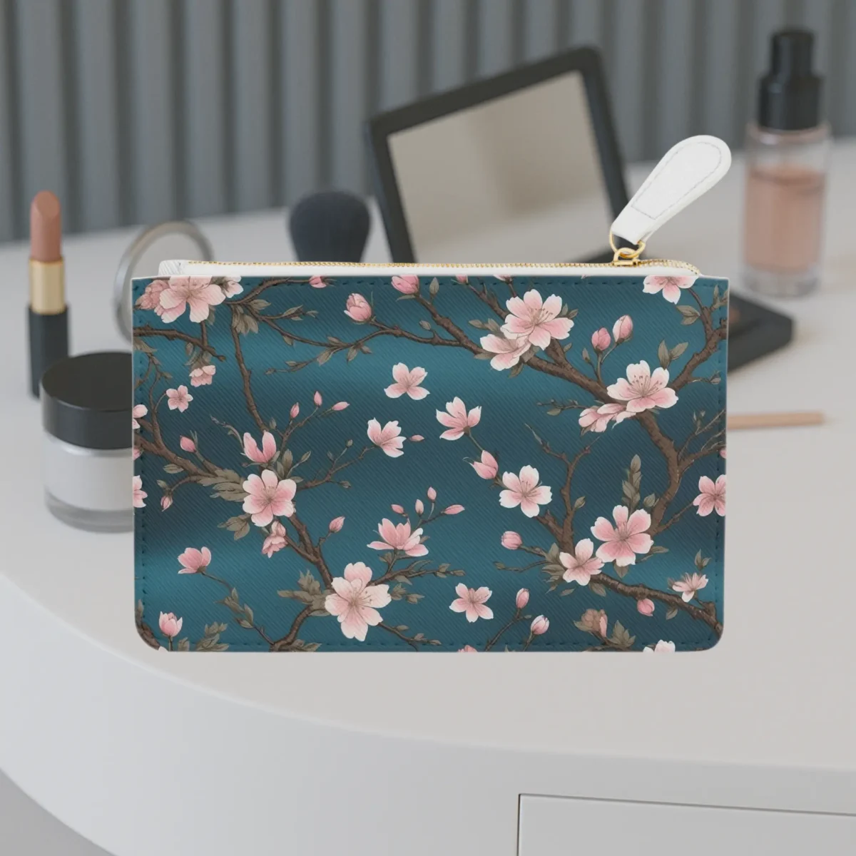 Mini clutch bag with a cherry blossom branch design on a deep teal background, displayed on a vanity table.
