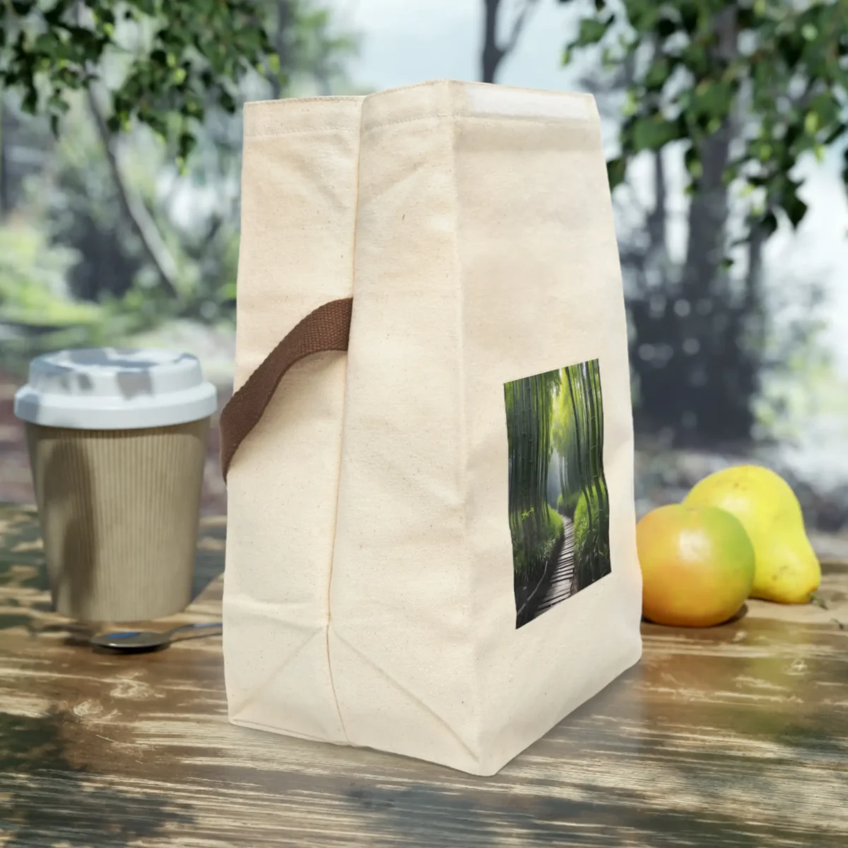 Side view of a cream canvas lunch bag with brown strap and a bamboo forest photo print, placed on an outdoor wooden table.