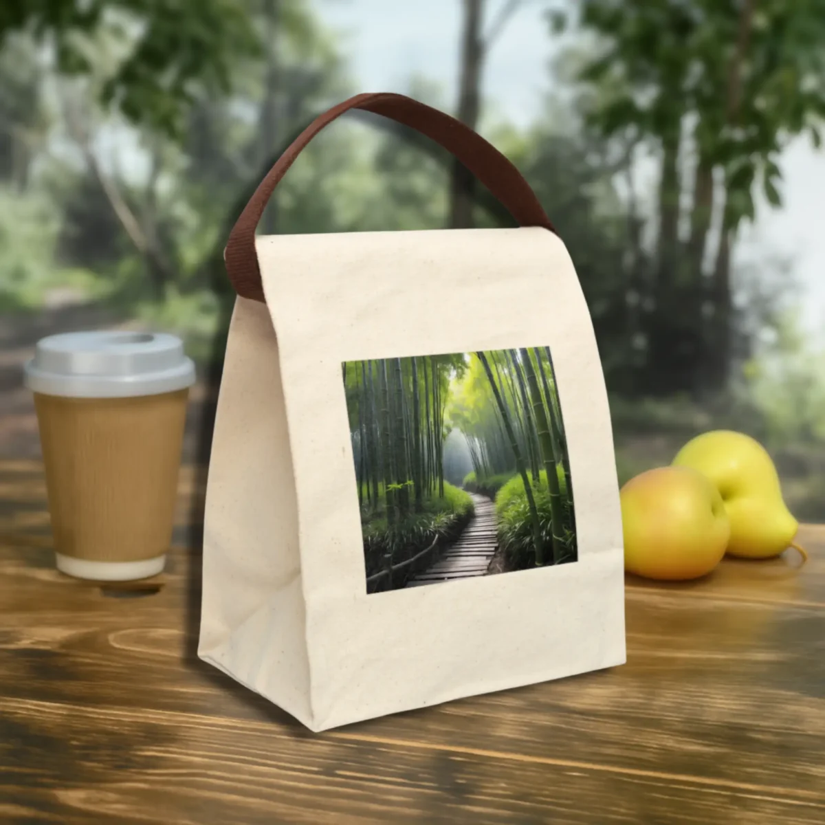 Canvas lunch bag with a calming bamboo forest print and brown handle, styled on an outdoor wooden table with fruits and coffee.