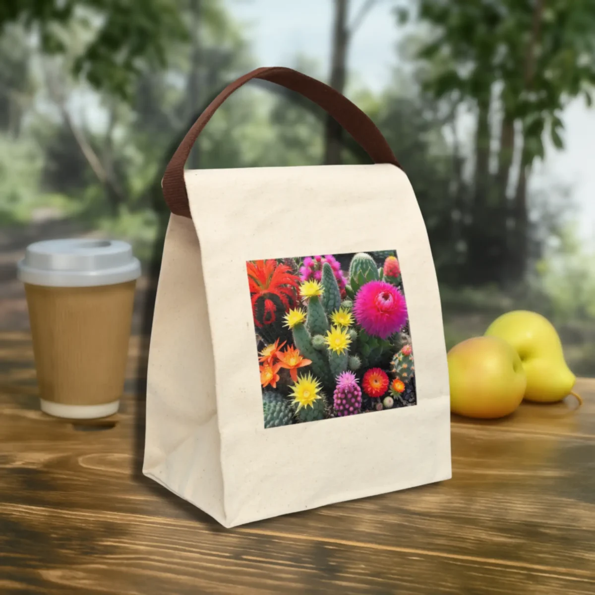 Front angle view of a canvas lunch bag with a colorful cactus garden print and brown strap, set on a wooden table outdoors.