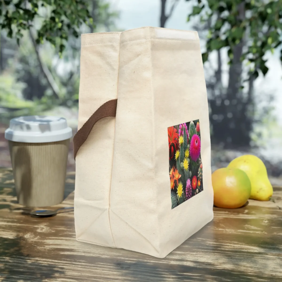 Side view of a cream canvas lunch bag with brown strap and vibrant cactus flower print, placed on a wooden outdoor table.