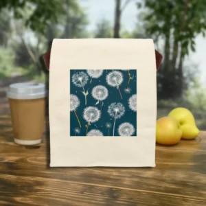 Flat front view of a canvas lunch bag with a white dandelion seed print on a teal background, shown outdoors on a wooden table.