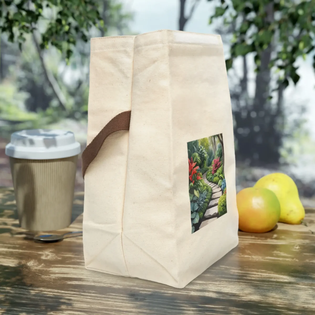 Side view of a cream canvas lunch bag with brown strap and garden pathway print, placed on a wooden outdoor table.
