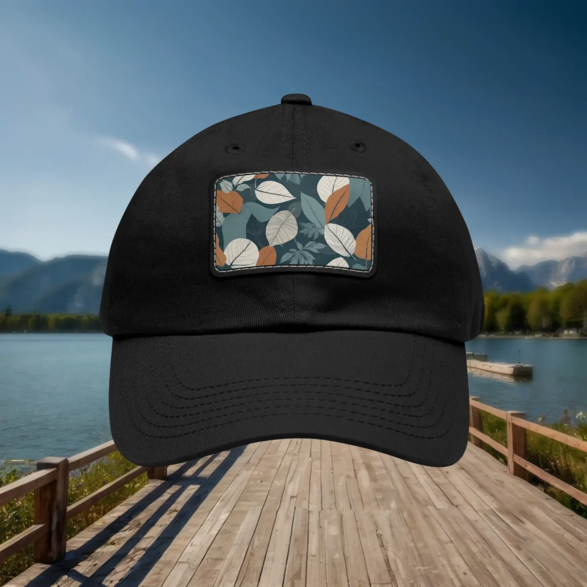 Close-up of black dad hat with autumn leaf pattern patch, outdoor lakeside background