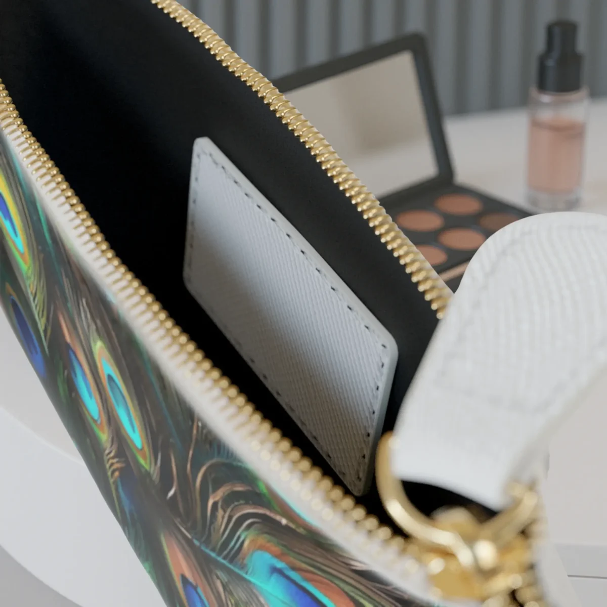 Interior of the mini clutch bag with a visible card pocket and peacock feather print along the edge