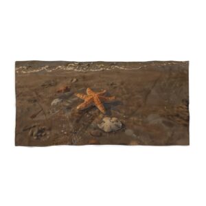 Beach towel with starfish and rocks near ocean waves on sandy shore