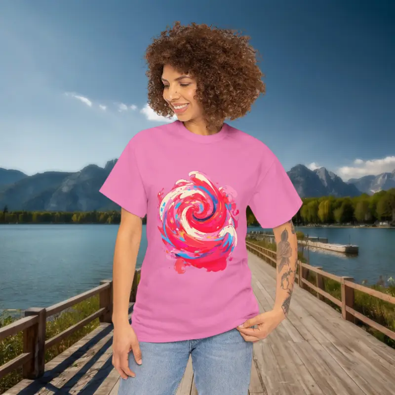 Bright Swirl Tee in Nature Smiling woman with curly hair wearing a pink t-shirt with a colorful swirl design by a lake and mountain range