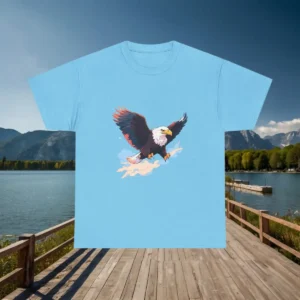 Flatlay of a light blue t-shirt with an illustrated bald eagle flying through clouds, displayed above a lakeside dock.