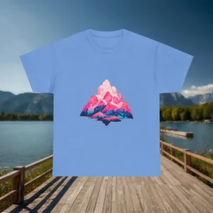 Flatlay of a light blue t-shirt with a pink and blue mountain range illustration, displayed against a mountain lake background.