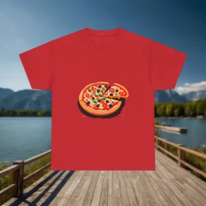 Flatlay of a red t-shirt featuring a cartoon-style pizza with a lifted slice and colorful toppings, displayed in front of a scenic lake and mountain backdrop.