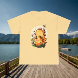 Flat lay of a yellow t-shirt with beehive and bees design, displayed on a pier with lake and mountain background.