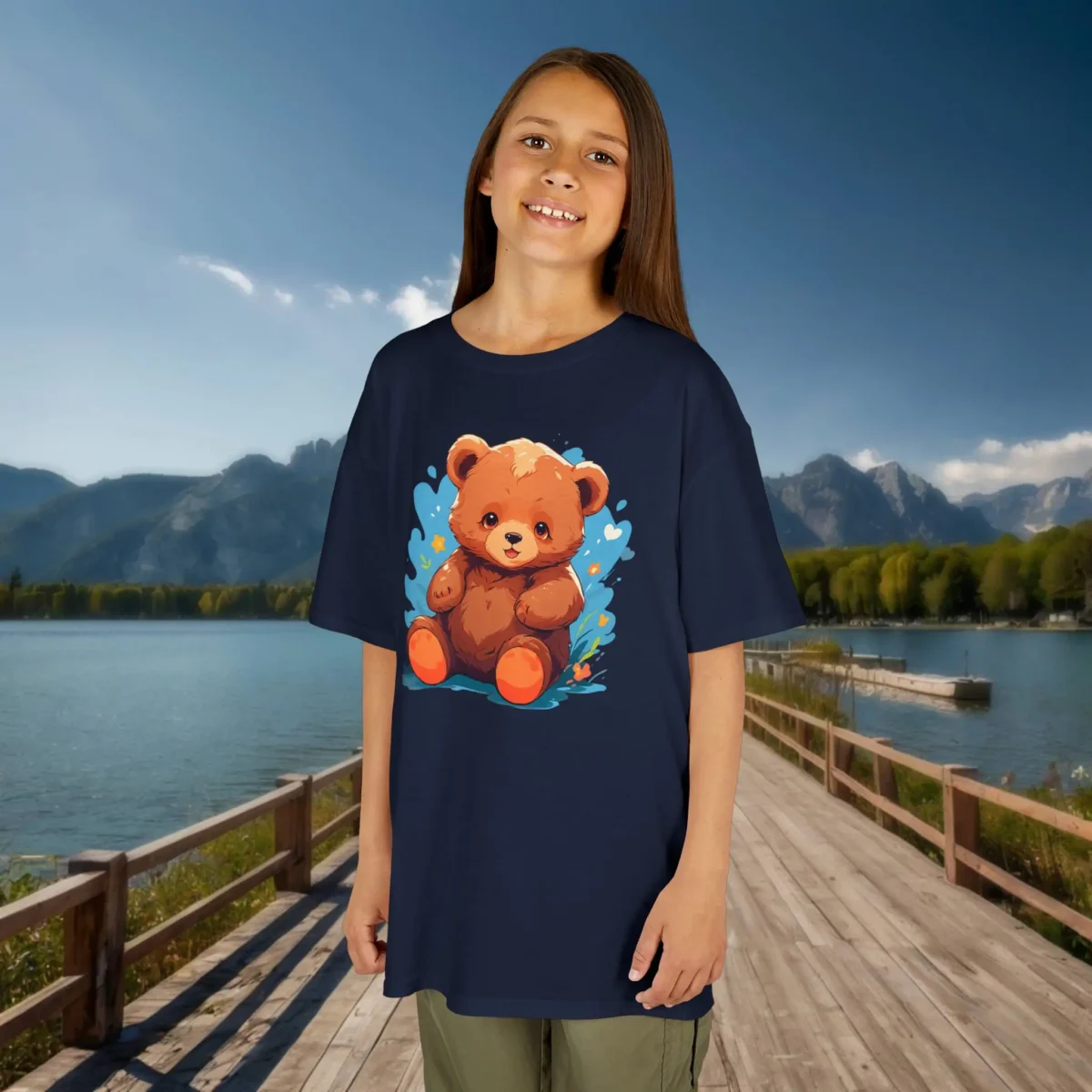 Girl wearing a navy blue t-shirt with a cute cartoon baby bear surrounded by blue hearts and stars, standing on a dock near a mountain lake.