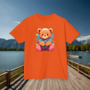 Front view of an orange kids t-shirt featuring a cartoon baby bear in bright clothing, displayed on a boardwalk by a lake.