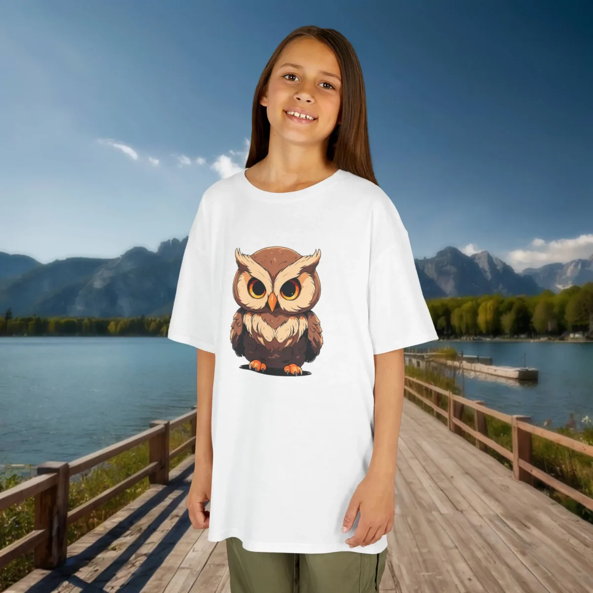 Girl wearing a white t-shirt with a cute cartoon baby owl with large eyes, standing outdoors by a mountain lake.