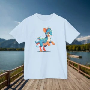 Front view of a sky blue kids t-shirt with a cartoon baby Gallimimus, displayed on a boardwalk by a lake and mountains.