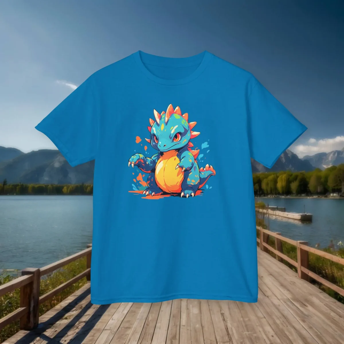 Flat lay of a sapphire blue kids T-shirt with a dynamic baby Therizinosaurus graphic, set on a wooden bridge near a lake and mountains.