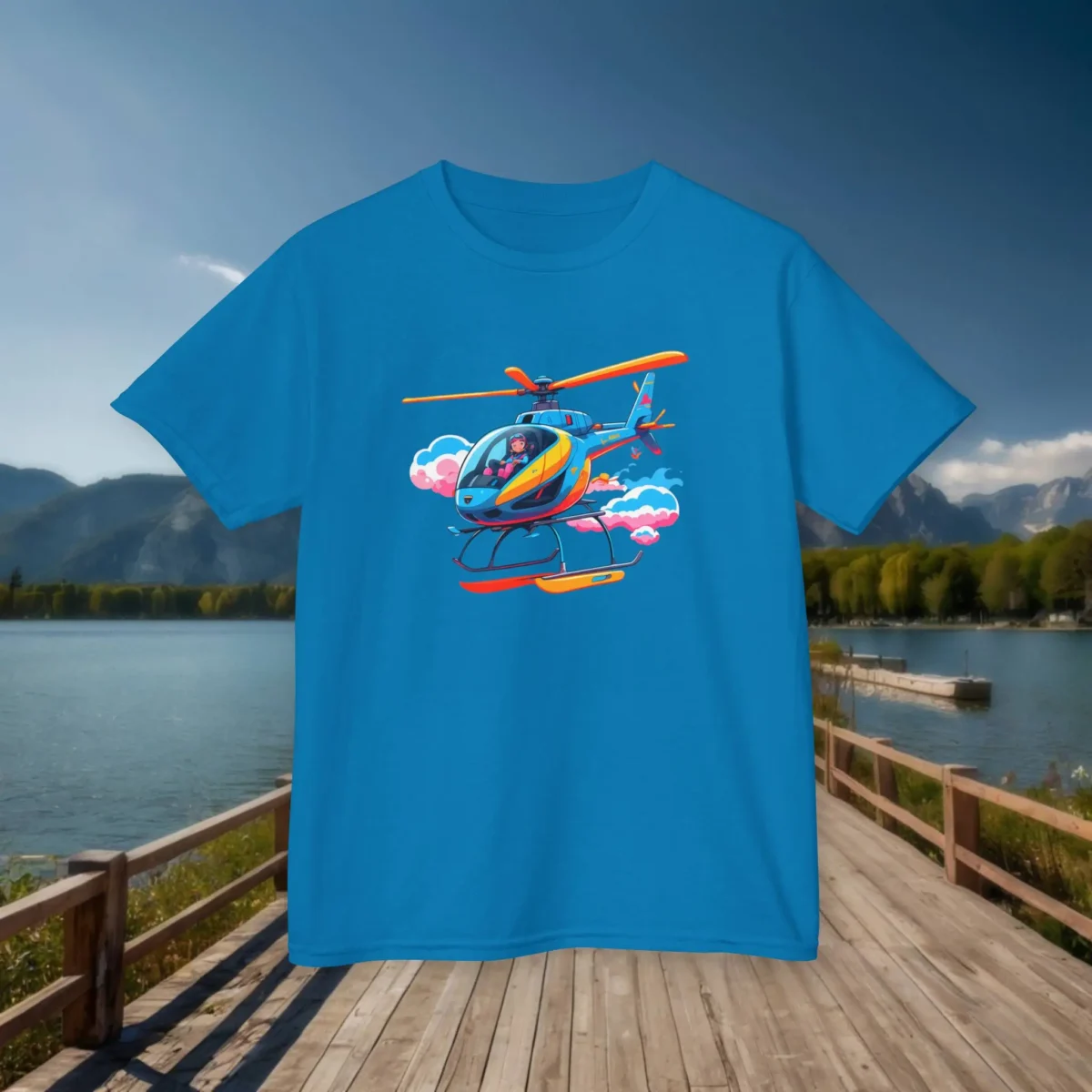 Flat lay of a sapphire blue kids t-shirt with a cartoon helicopter flying through clouds, displayed on a lakeside wooden dock.