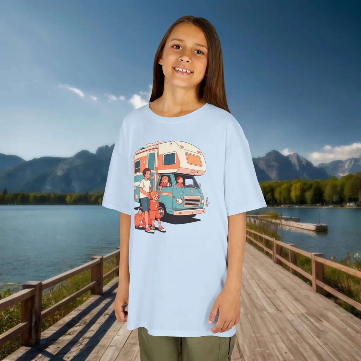 Girl wearing a light blue t-shirt featuring a cartoon-style family RV trip illustration, standing on a dock by a lake.