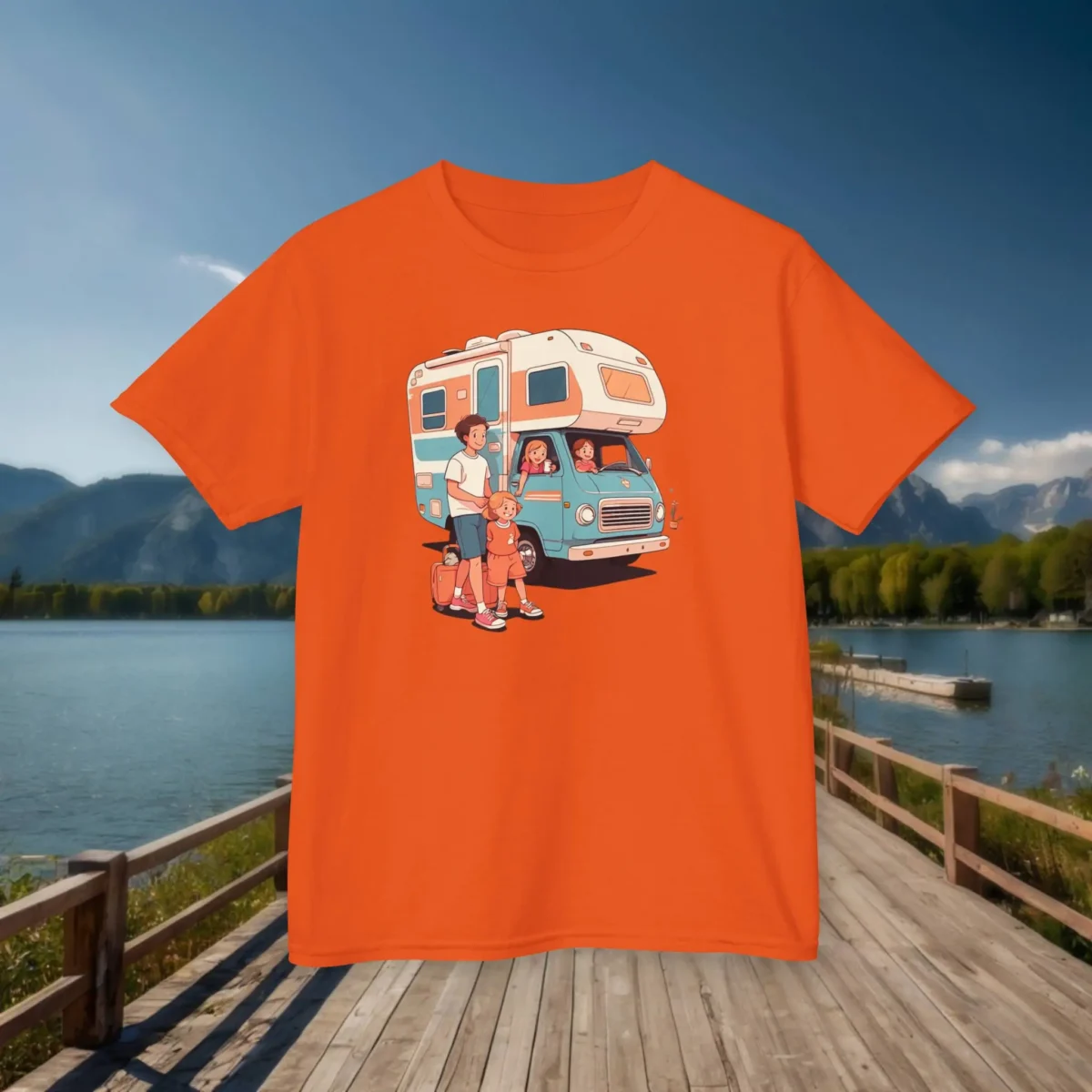 Flat lay of an orange kids t-shirt with a cartoon RV and family trip illustration, placed on a dock with mountains and lake in the background.