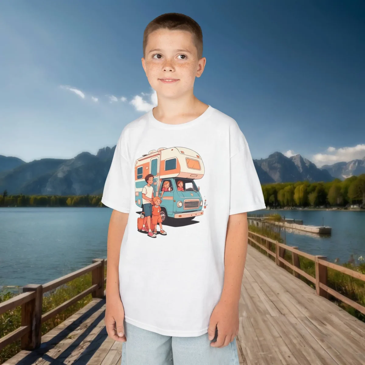 Boy wearing a white kids t-shirt with a cartoon-style family RV vacation design, standing near a scenic mountain lake.