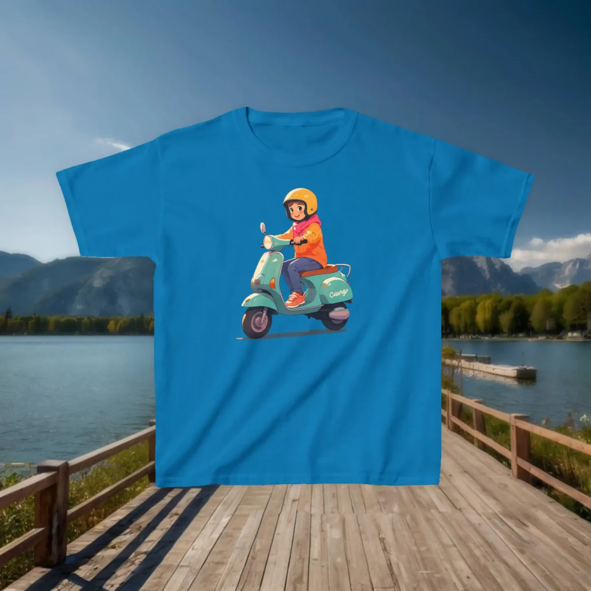 Flat lay of a sapphire blue kids t-shirt with a cartoon illustration of a girl riding a vintage scooter, placed on a dock by a lake.